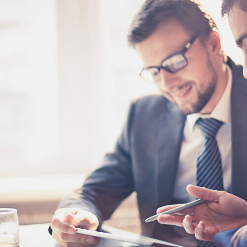 Image of two young businessmen using touchpad at meeting